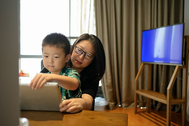 The mother was playing the tablet computer with her son in the living room